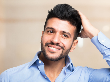 Smiling man in a blue shirt with hand in his hair against a light background
