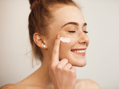 Woman applying cream to her cheek, smiling in a close-up skincare routine