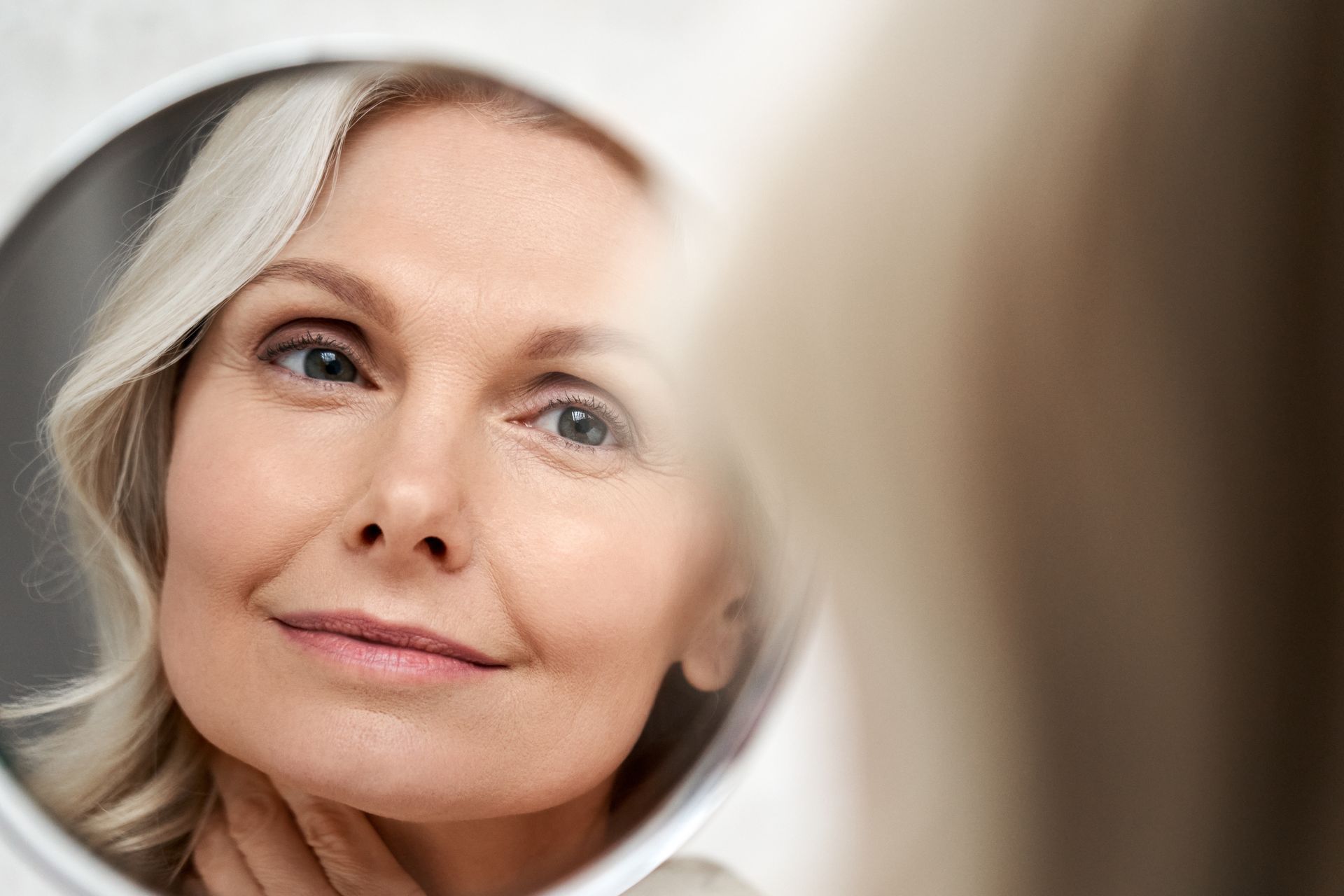 Close-up of a person looking into a mirror with a slight smile, soft focus in the foreground