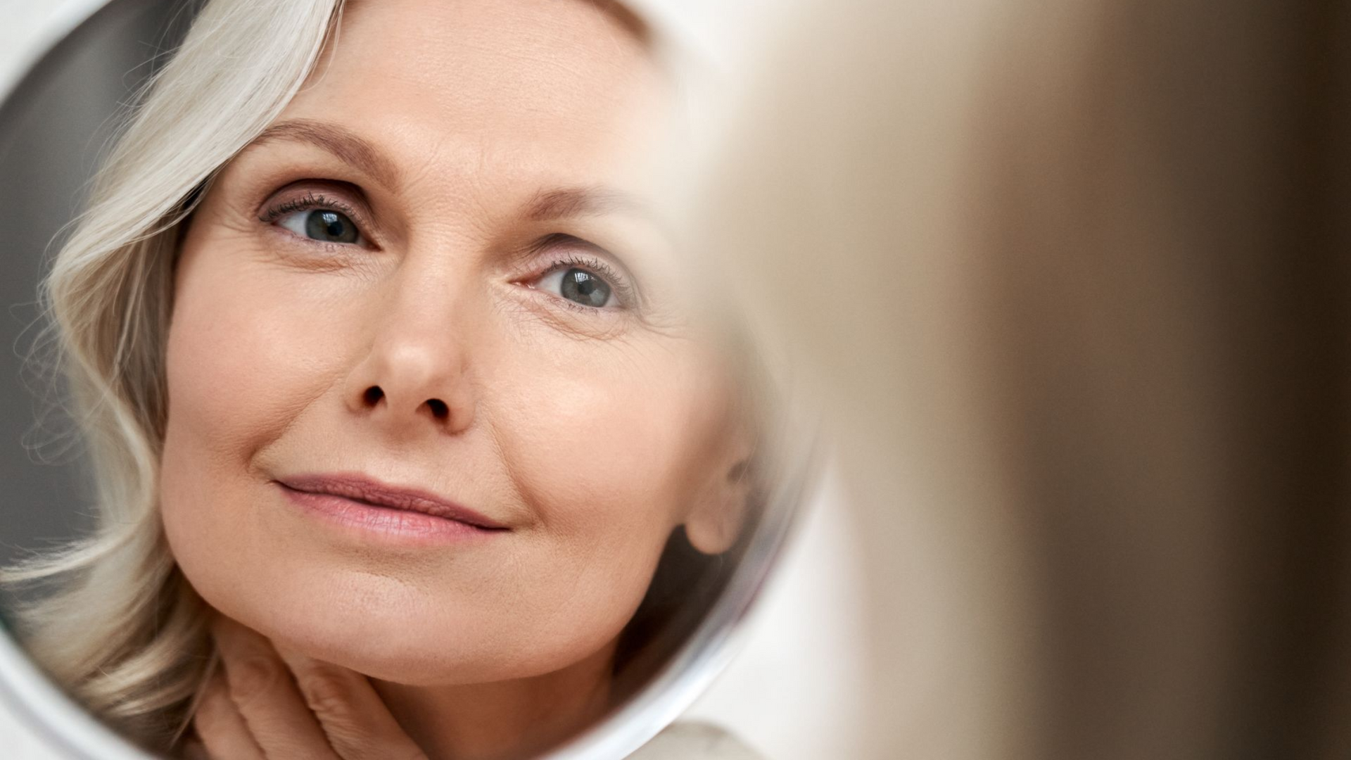 Close-up of a woman with short gray hair looking into a mirror, softly lit.
