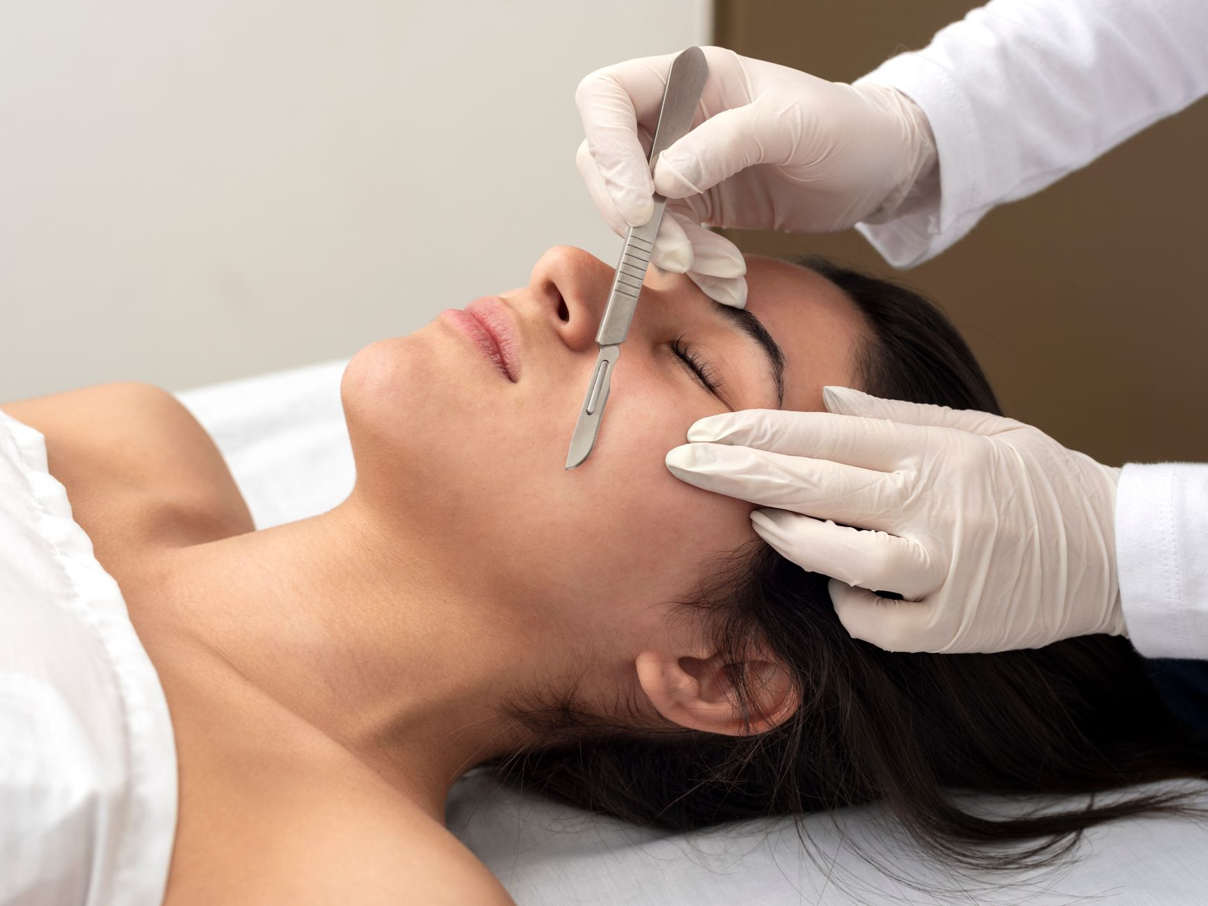 Aesthetician measuring a client’s eyebrow with a brow caliper during a beauty treatment