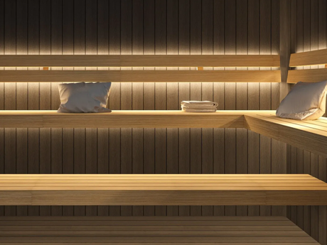 Warm-lit wooden sauna interior with bench seating, pillows, and folded towels.
