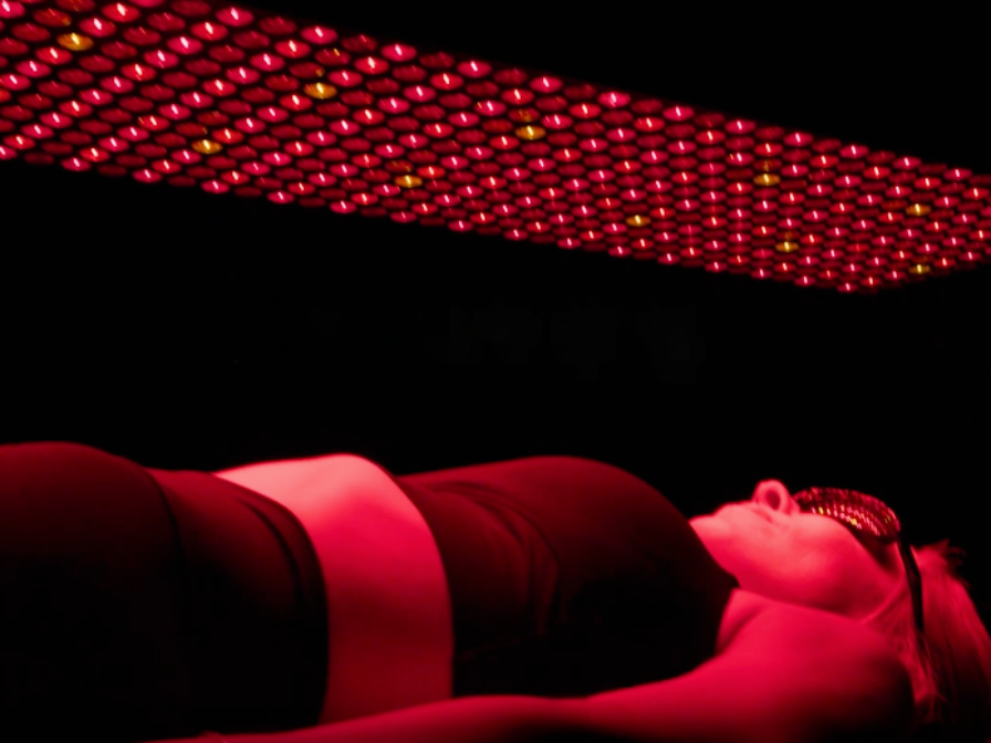 Person lying under a red LED light panel in a dark room