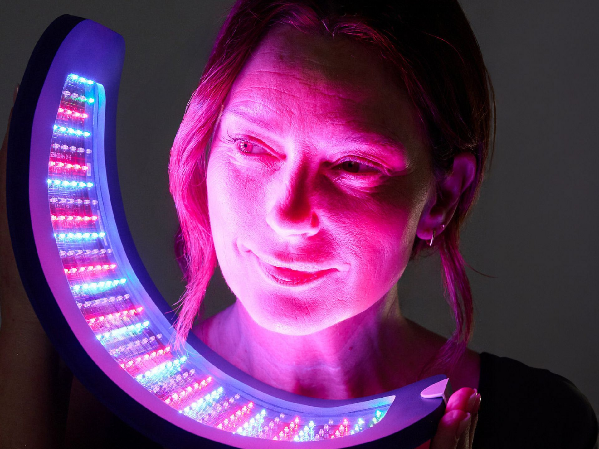 Woman lit by pink light beside a curved neon LED ring