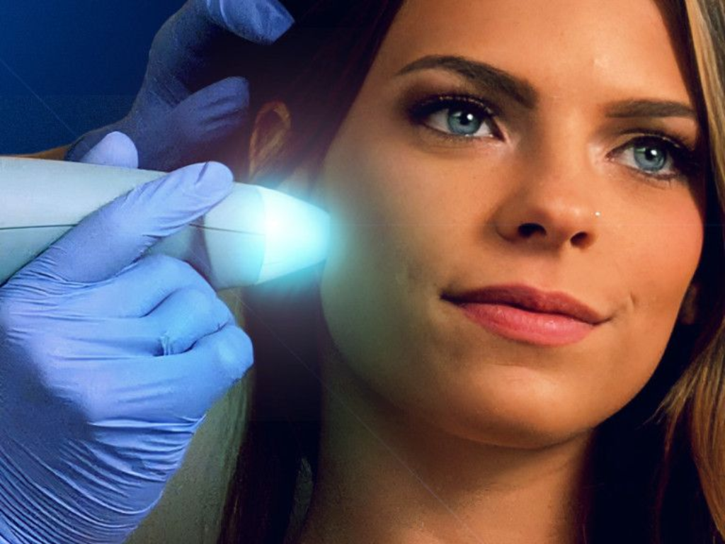 Gloved hand holding a glowing device near a woman’s face in a dark setting