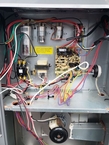Outdoor HVAC unit with exposed service gauges and hoses beside a house and trash bins