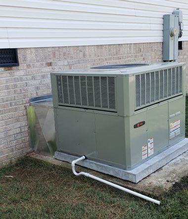 Outdoor air conditioner unit beside a brick wall, surrounded by mulch and shrubs