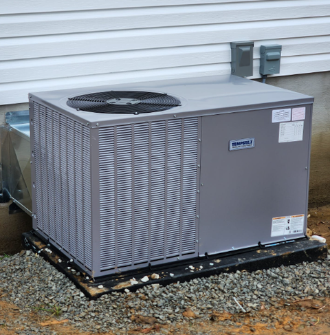 Gray outdoor HVAC unit on gravel beside a building, with a top-mounted fan.