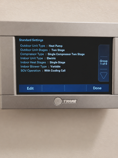 Wall-mounted white thermostat with digital display on a beige wall near a doorway