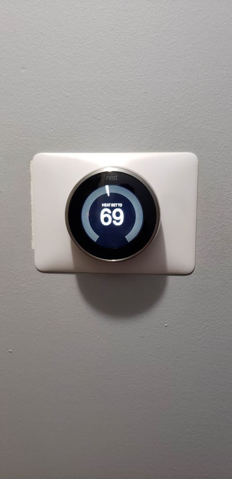 Hand pressing a doorbell on a white wall near a bright living room