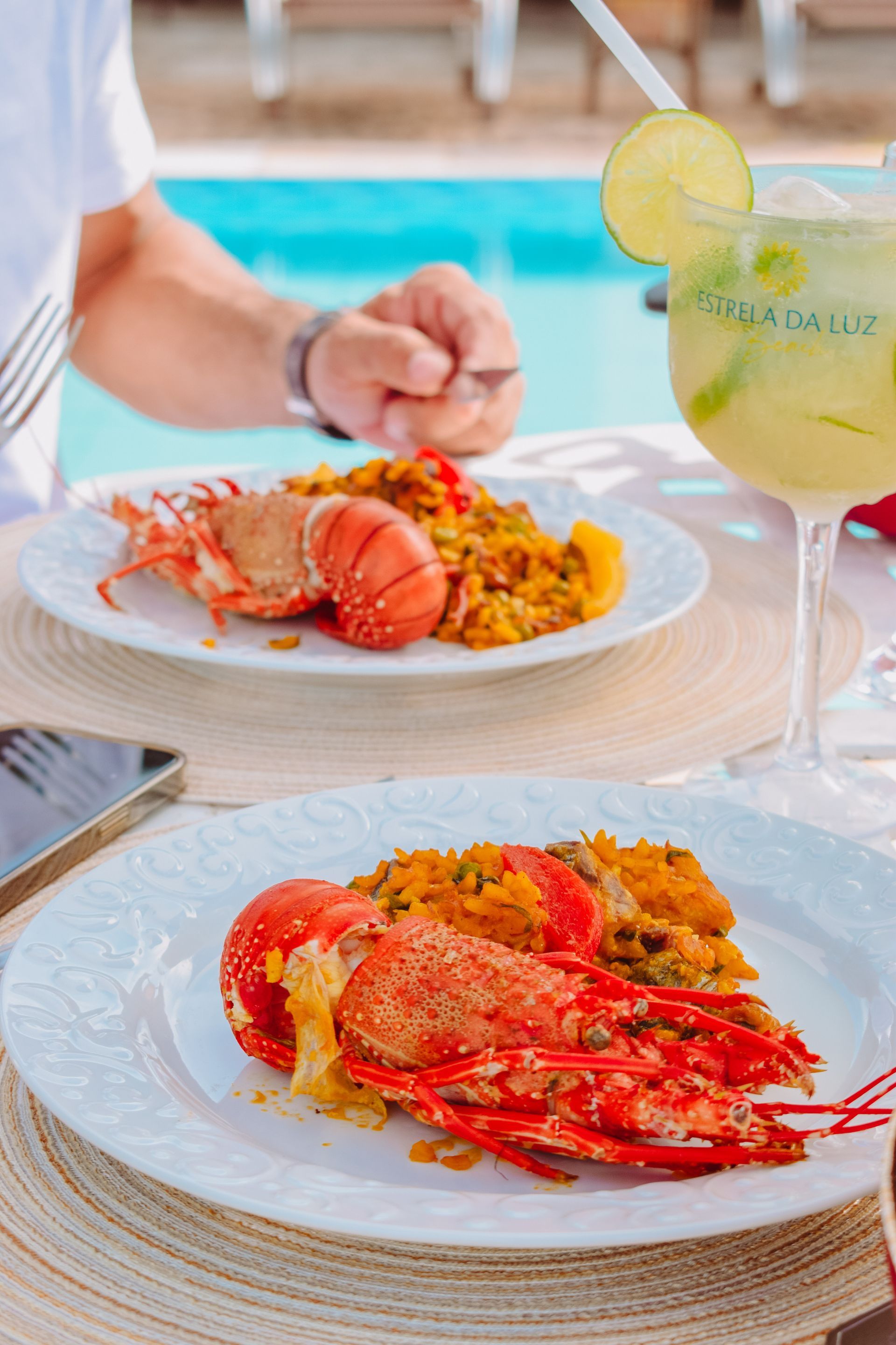 A man is sitting at a table with two plates of food and a drink.