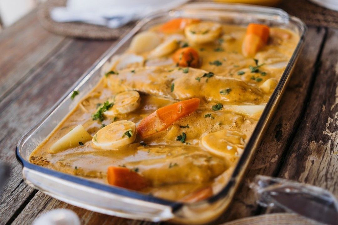 A casserole dish filled with chicken and carrots on a wooden table.