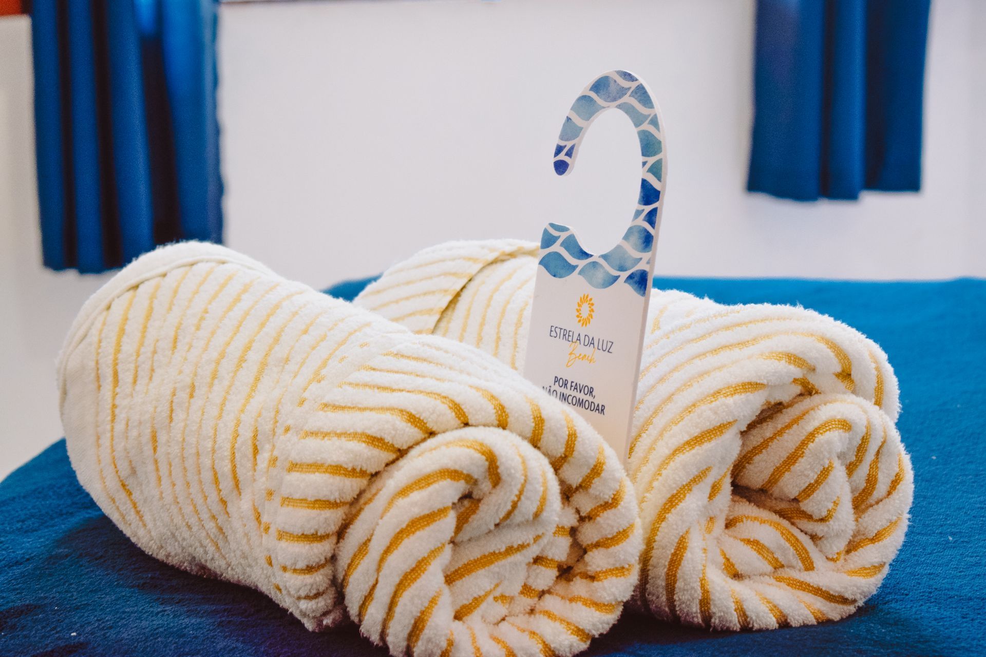 Two towels are rolled up on a bed next to a door hanger.