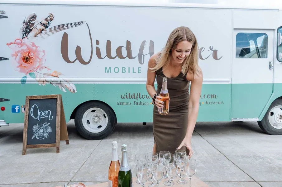 Ladies night, woman pouring champagne in front of a Wildflower Fashion truck