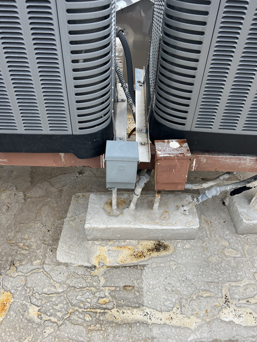 HVAC units on a rooftop, with electrical boxes and supports attached to a concrete base.