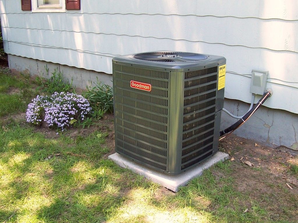 Air conditioning unit on a concrete pad next to a white house with landscaping.