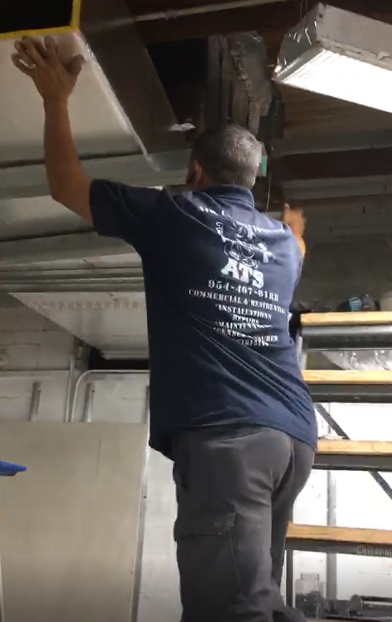 Man in blue shirt on a step ladder, installing a ceiling panel in a garage.