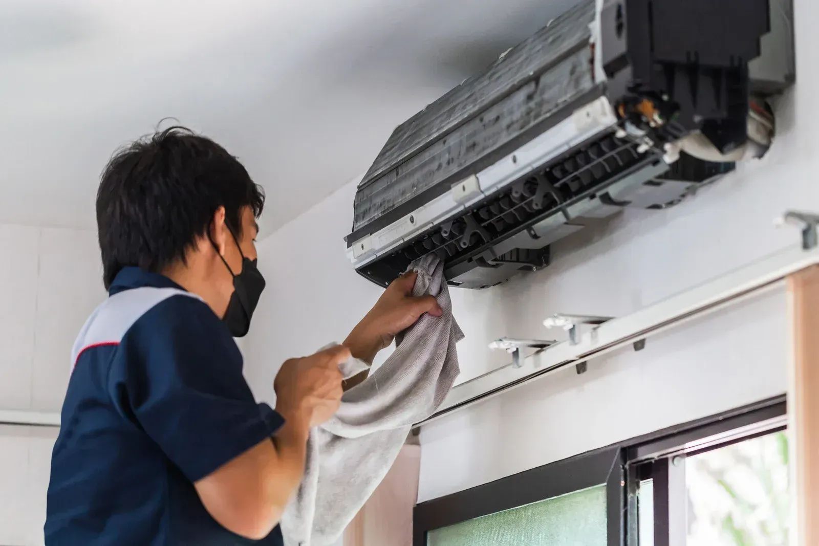 Technician cleaning an air conditioning unit indoors.