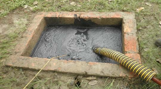 Una persona está bombeando una manguera a un tanque séptico.