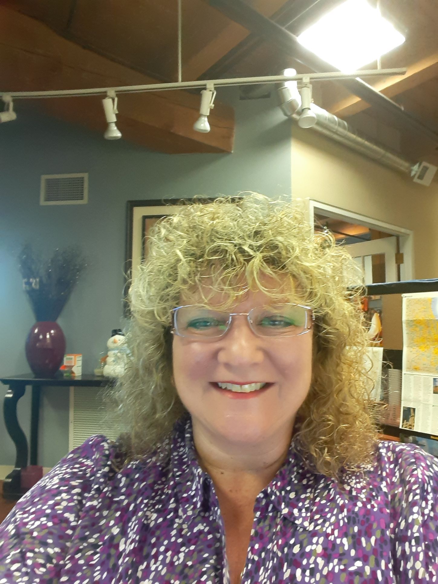 A woman wearing glasses and a purple shirt is smiling for the camera.