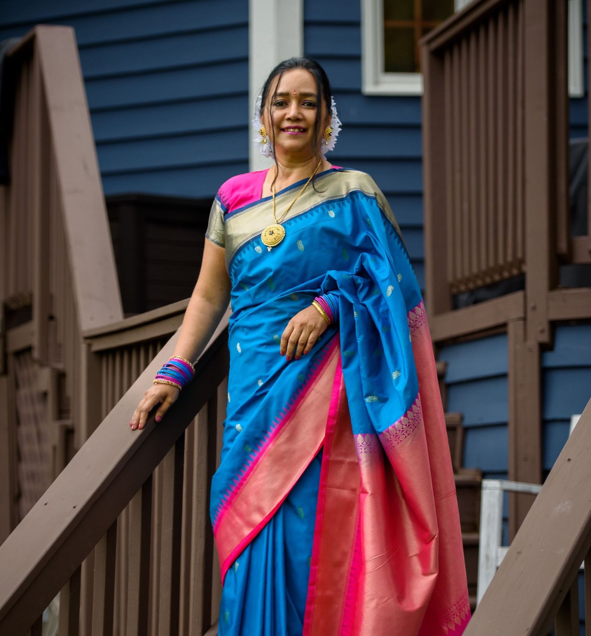A woman in a blue and pink saree is standing on a set of stairs.