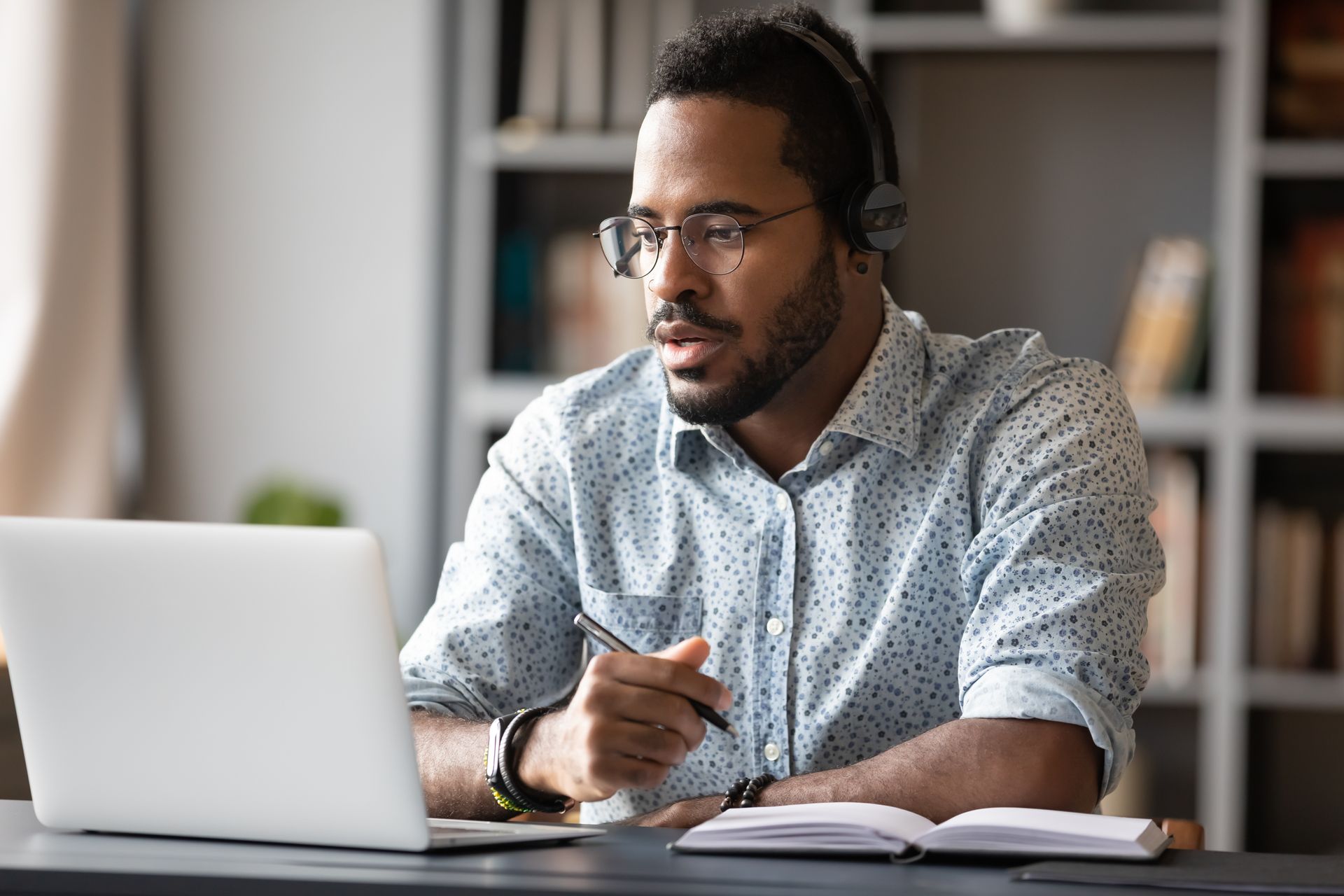 A man wearing headphones is sitting at a desk using a laptop computer.