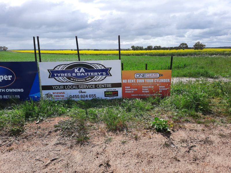 Promotional signs in a grassy field beside a yellow crop field under a cloudy sky