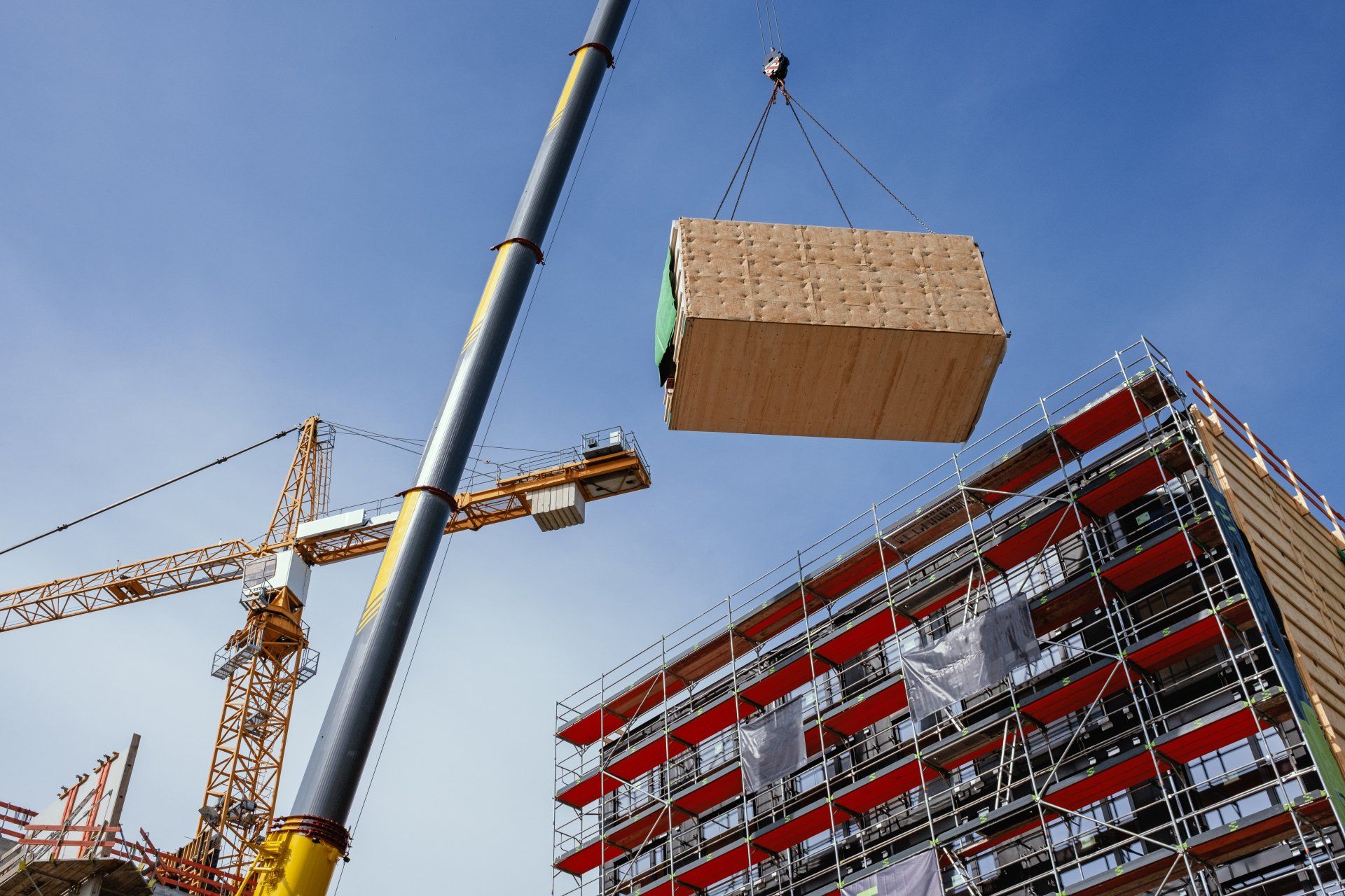 Crane lifting a wooden building module to its position in the structure. Construction site of an office building in Berlin. The new structure will be built in modular timber construction.