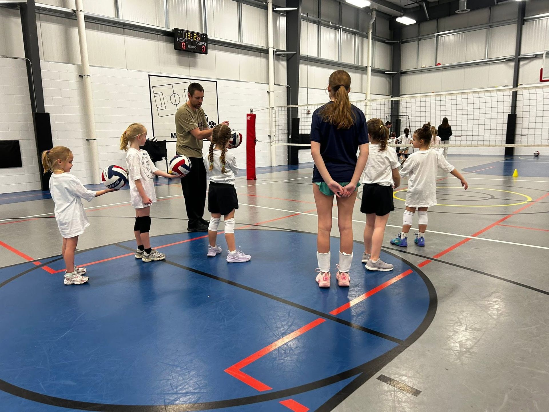 Children in a volleyball camp standing in a circle with instructors on a blue space during an activity