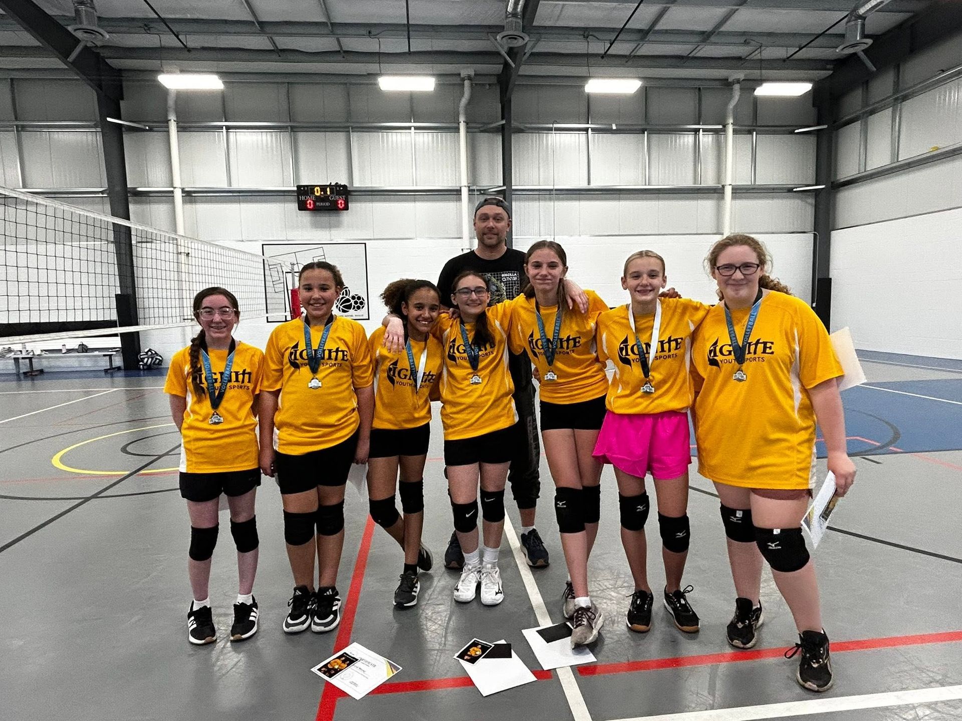 Youth volleyball team posing in yellow jerseys and black gear inside an indoor gym.