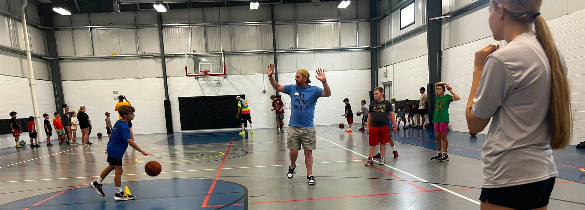 Children playing basketball in an indoor gym, with a coach watching nearby.