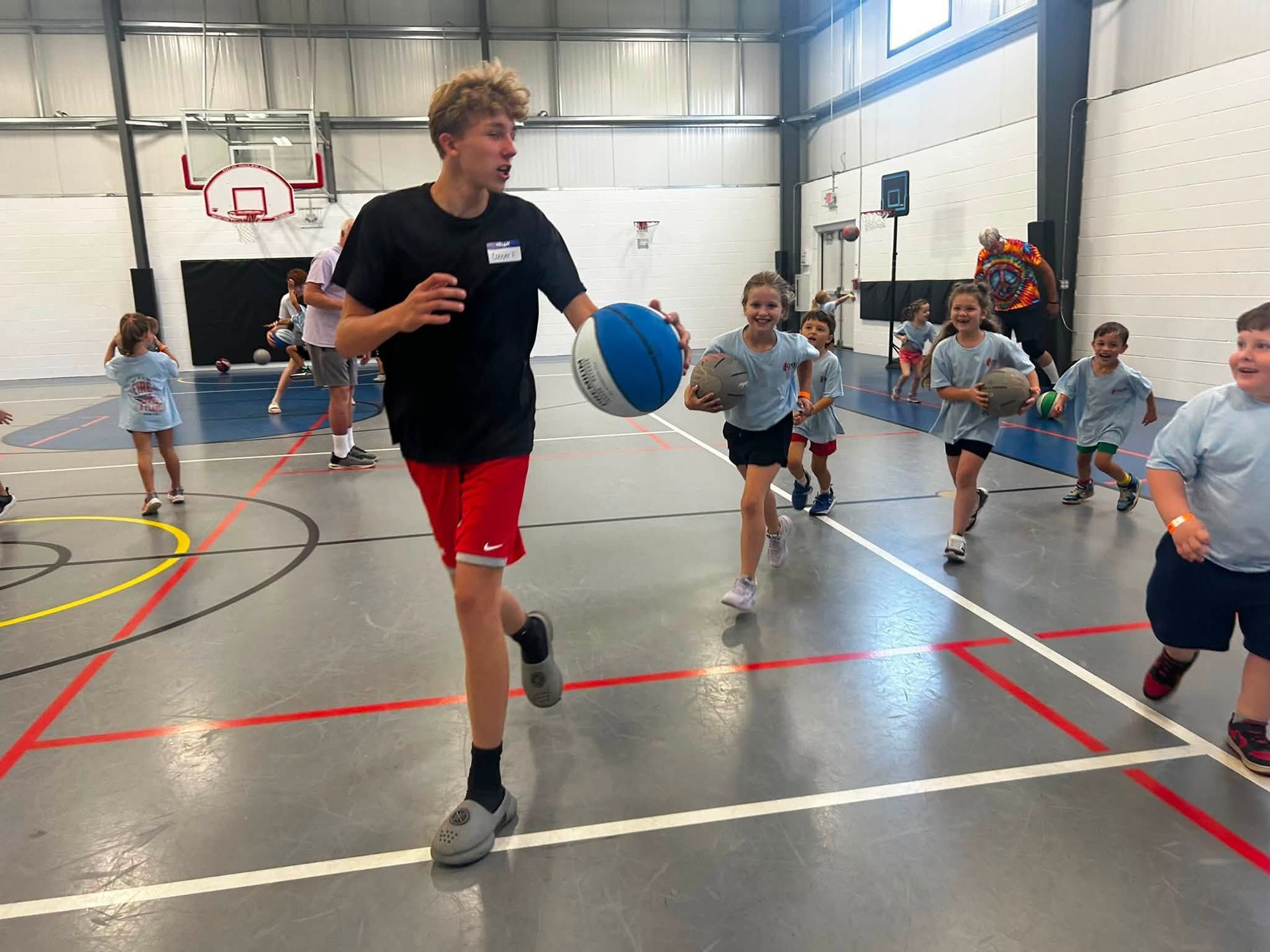 Children running drills in a gym, with one player dribbling a blue basketball in the foreground.