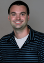 Smiling man in a dark striped polo shirt against a plain gray background