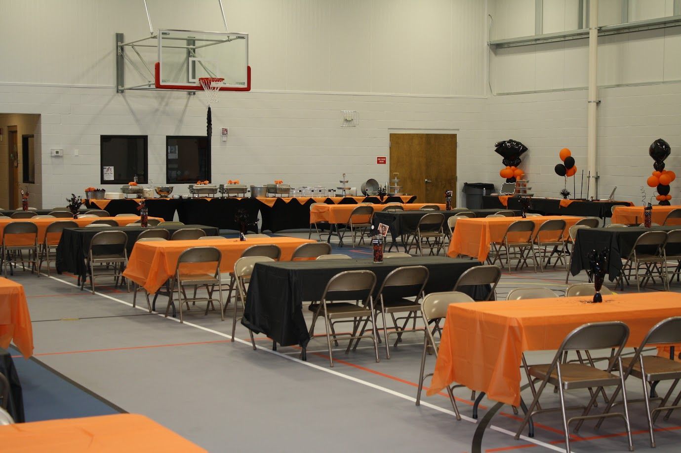 Empty gymnasium set up with tables and chairs draped in orange tablecloths for an event