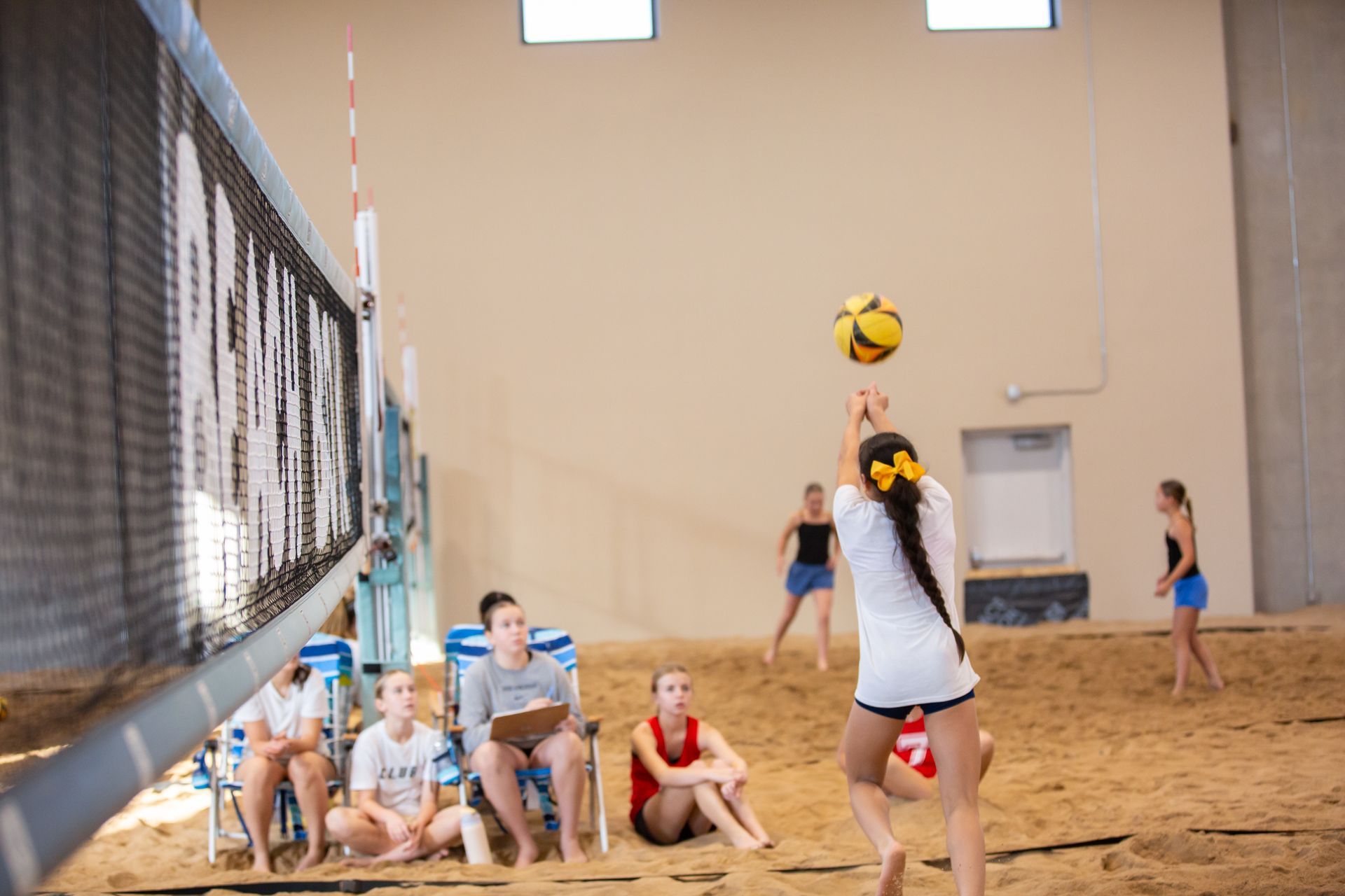 Three men on a sandy volleyball court, one shaking hands with another while a third looks on.