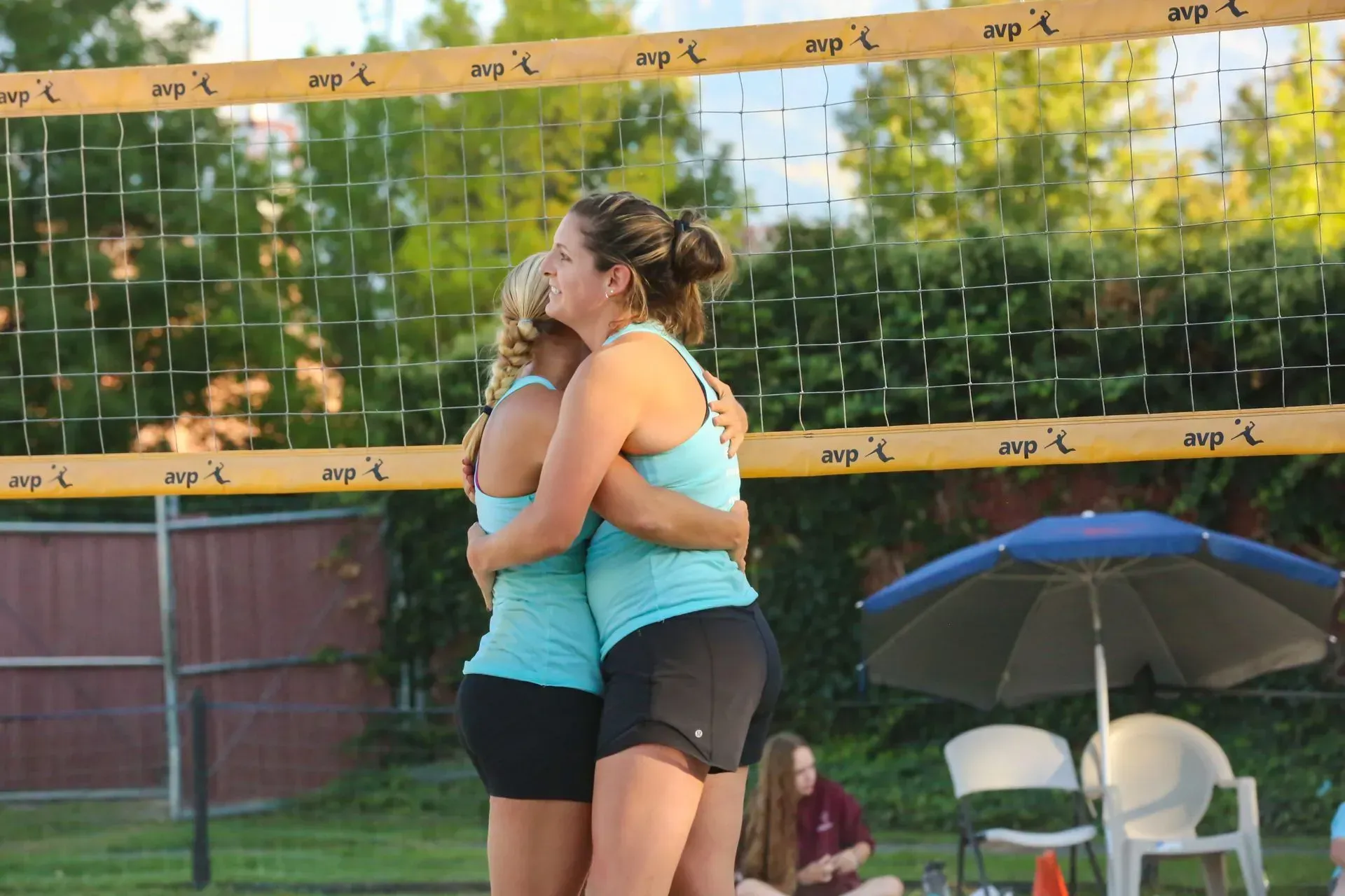 Two volleyball players in teal tank tops and shorts embrace at the net. Two volleyball players in teal tank tops and shorts embrace at the net.