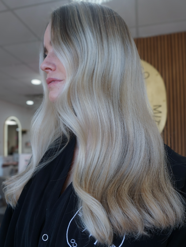 Side profile of a person with long platinum blonde hair in a softly lit indoor setting.