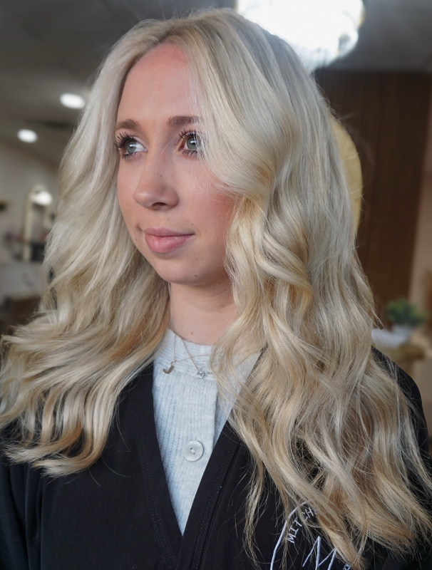 Blonde woman in a dark blazer, looking left indoors with soft lighting.