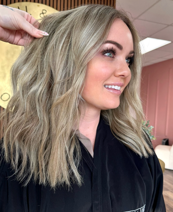Woman with shoulder-length wavy blonde hair in a salon, shown in side profile smiling softly