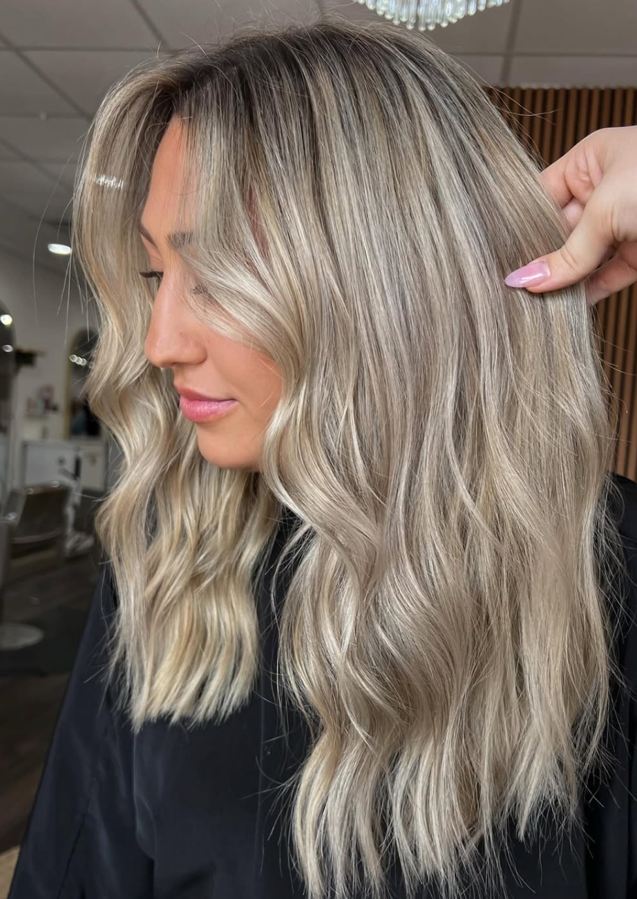 Side-view close-up of wavy platinum blonde hair with dark roots and layered ends in a salon.