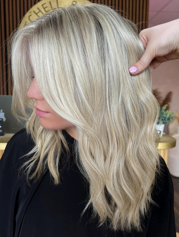 Side-profile of a person with layered platinum-blonde hair and dark roots, wearing a black top.