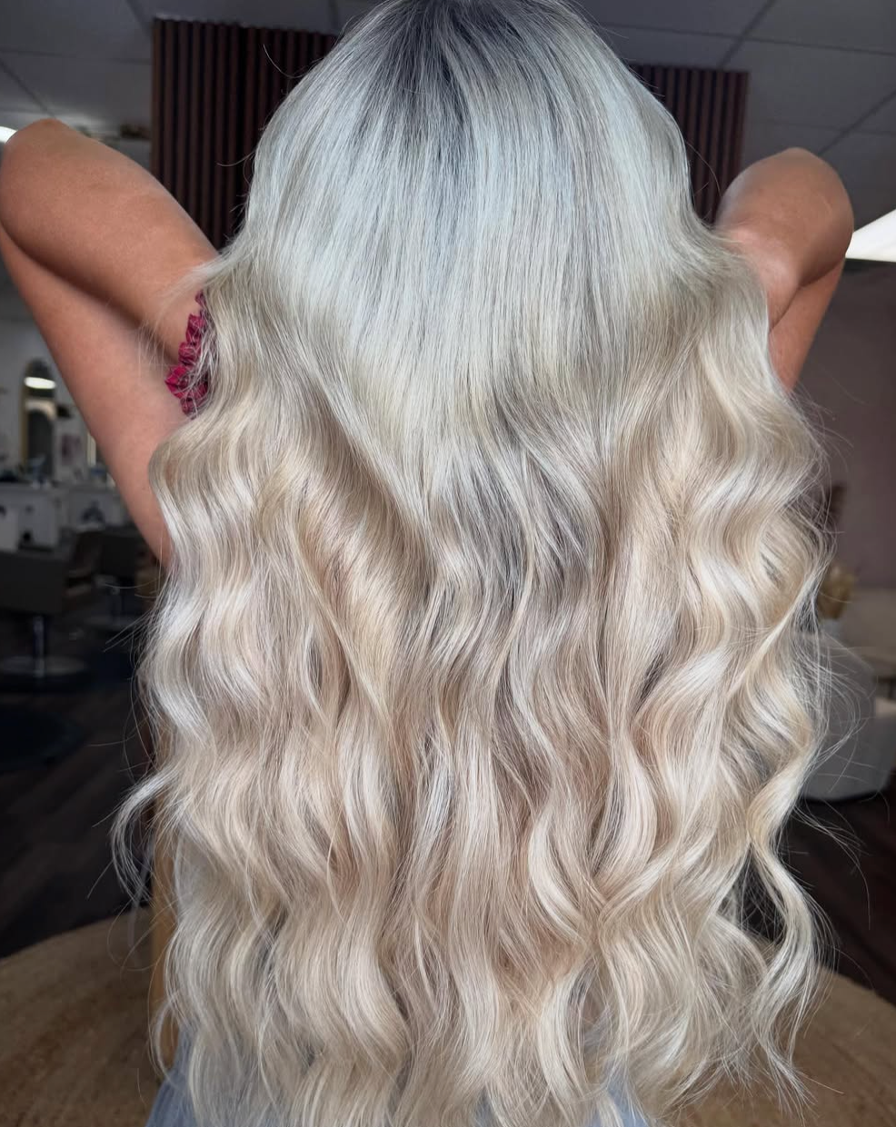 Long wavy platinum-blonde hair cascading down a person’s back, arms raised