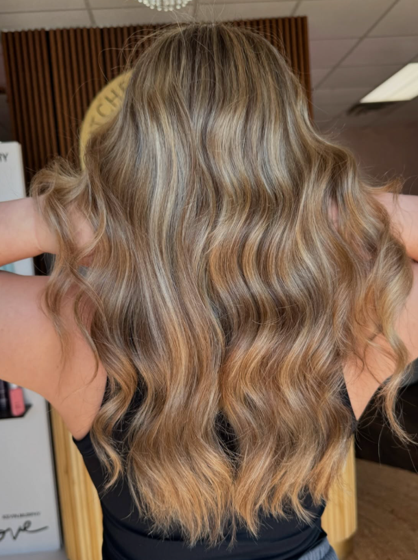 Wavy blonde hair with warm caramel highlights, shown from the back in a salon setting