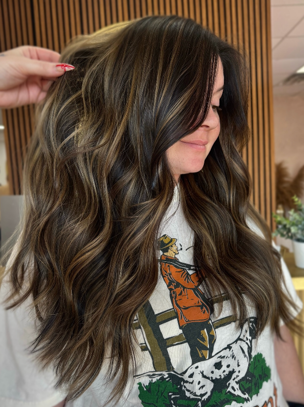 Woman with long wavy brown hair and blonde highlights, wearing a graphic tee indoors