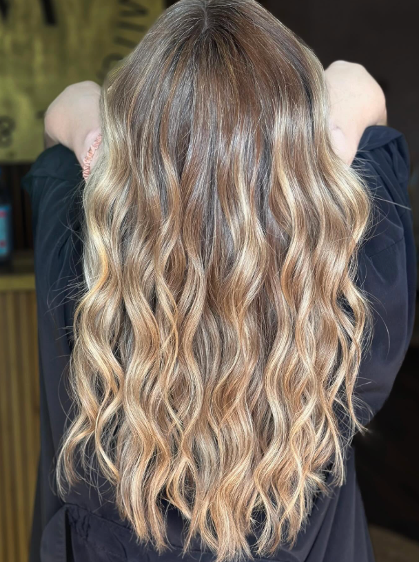 Back view of wavy blonde hair with darker roots, falling to mid-back.
