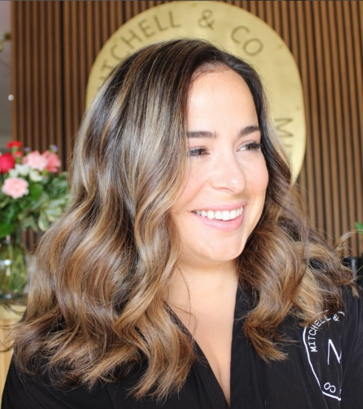 Smiling woman with wavy brown hair in front of a circular sign and flowers
