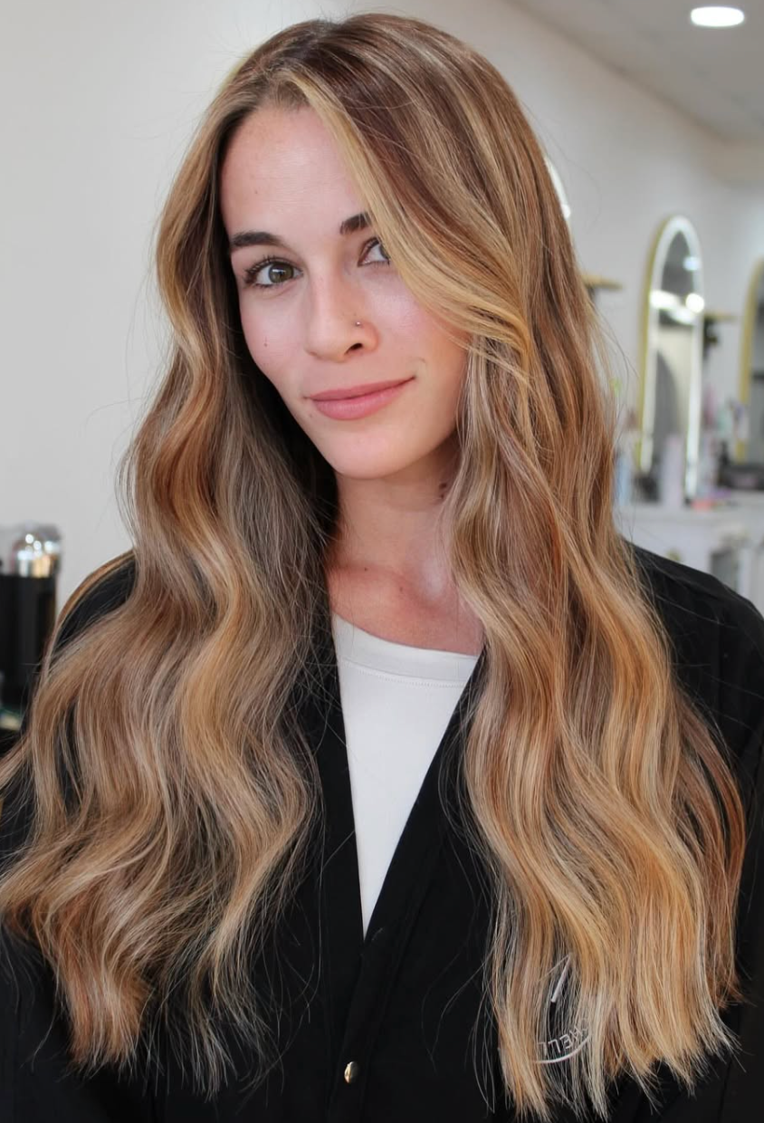 Portrait of a person with long wavy blonde hair in a black top, standing indoors in a salon