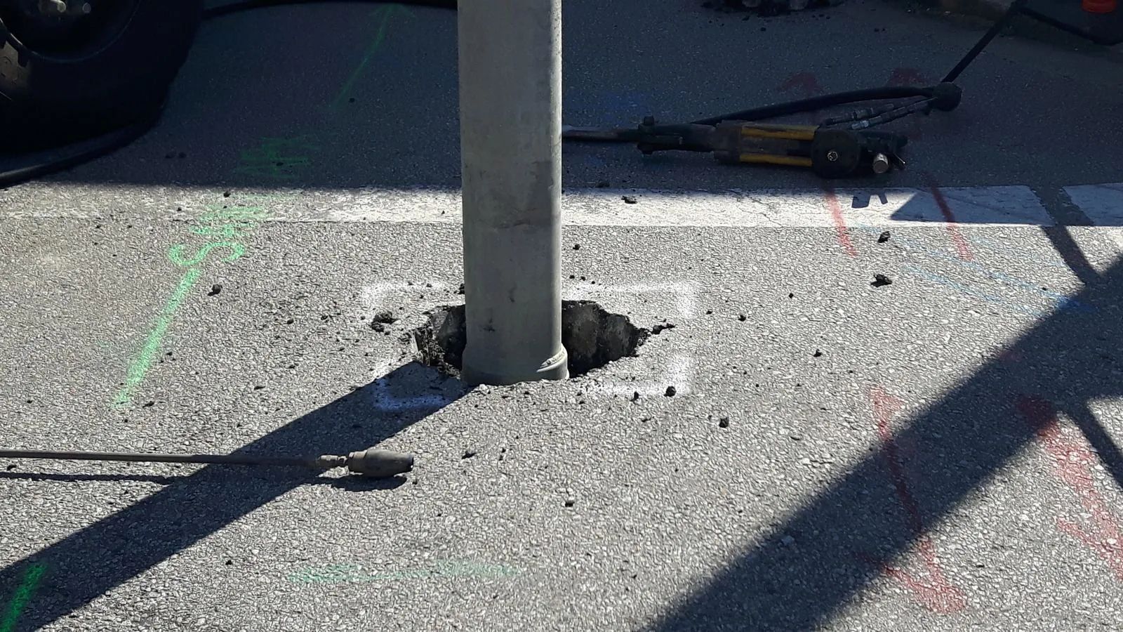 Metal pole set in asphalt; hole and tools visible.