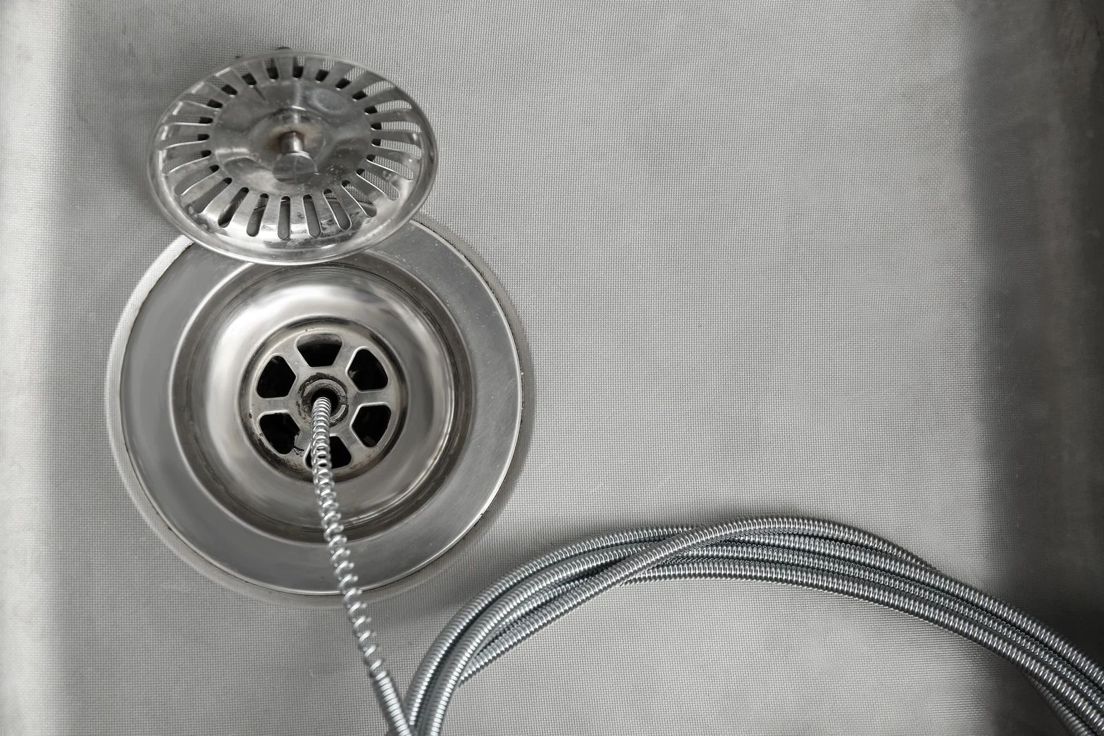 Close-up of a metal sink drain with a braided hose and circular drain cover on a textured basin.