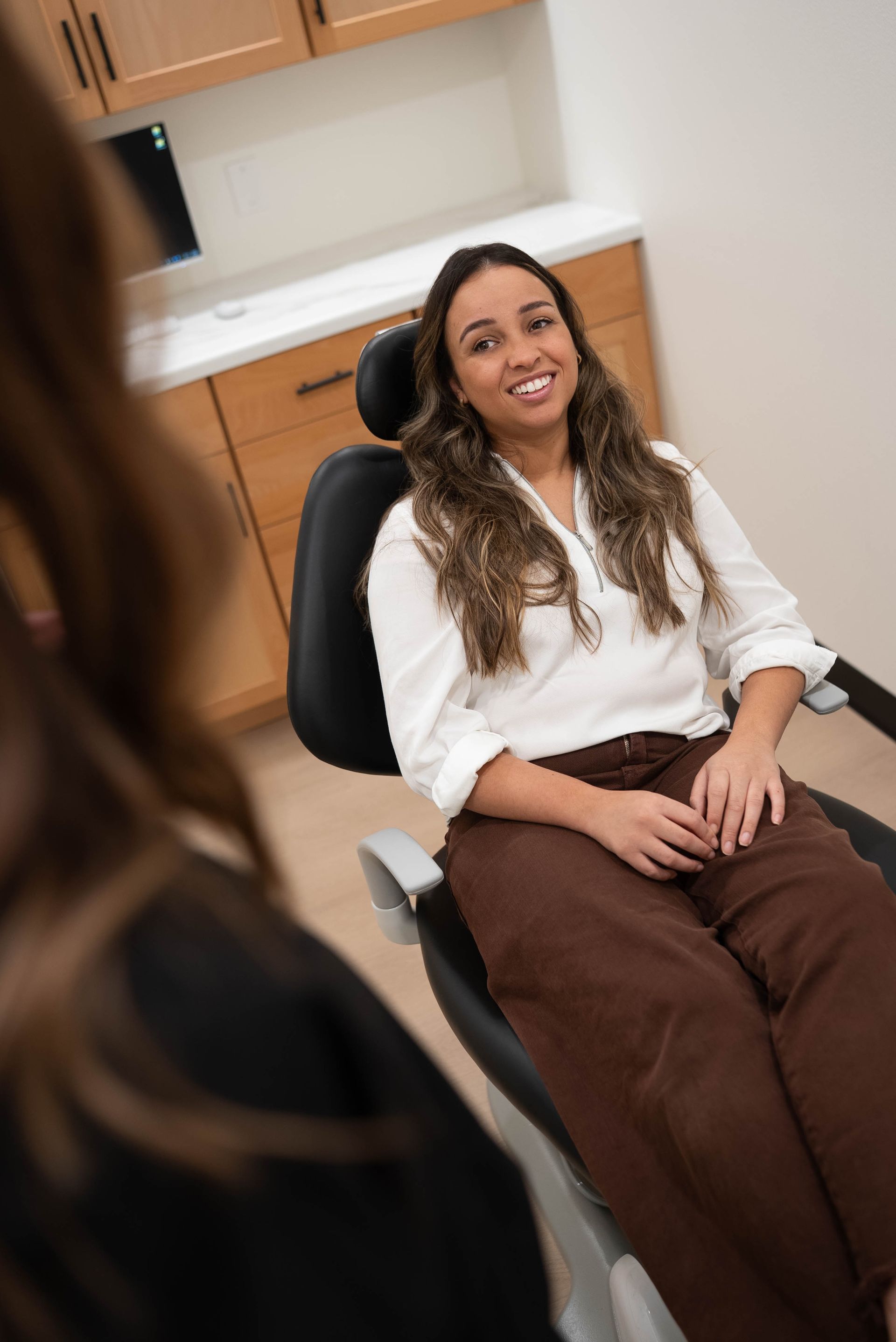 Smiling woman seated in a dental chair during an exam, with a staff member nearby